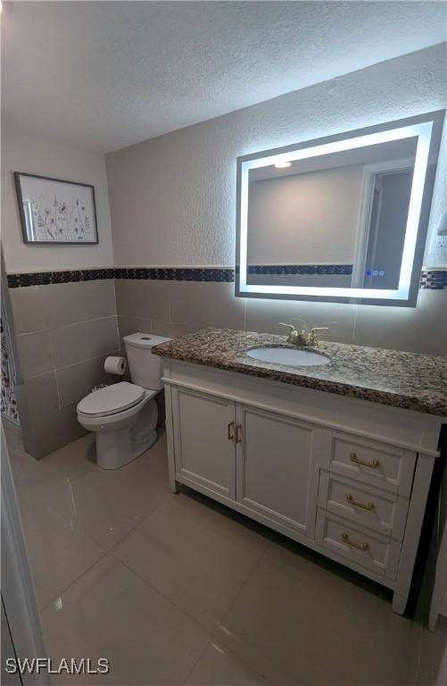 half bathroom with vanity, tile patterned flooring, a textured ceiling, tile walls, and toilet