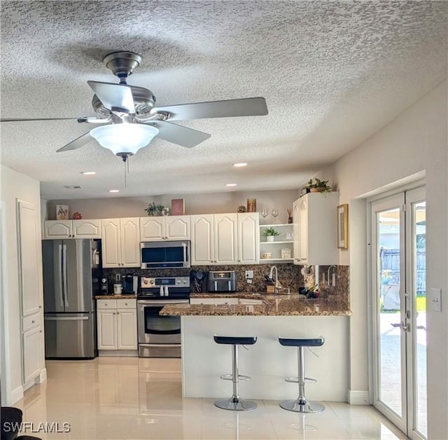 kitchen featuring a breakfast bar, open shelves, a peninsula, stainless steel appliances, and tasteful backsplash