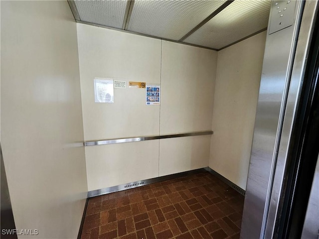 interior space with elevator, baseboards, and brick floor