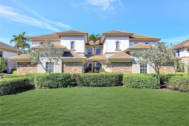 mediterranean / spanish-style home featuring a front lawn, a tiled roof, stone siding, and stucco siding