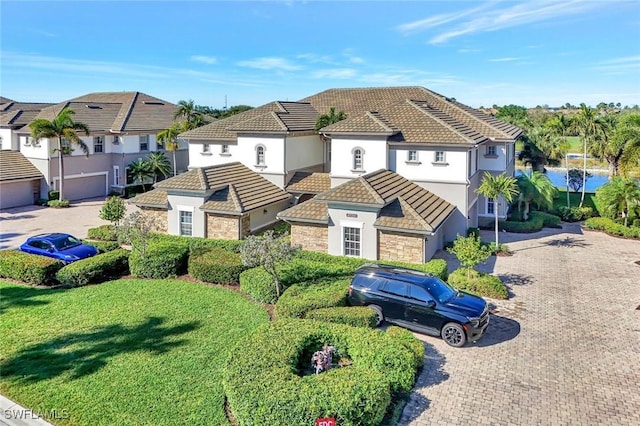 mediterranean / spanish house featuring a front lawn, a tiled roof, stucco siding, stone siding, and driveway