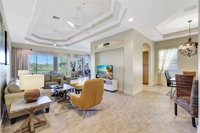 living area with visible vents, baseboards, ceiling fan with notable chandelier, arched walkways, and a raised ceiling