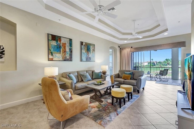 living room with light tile patterned floors, a tray ceiling, ceiling fan, and ornamental molding