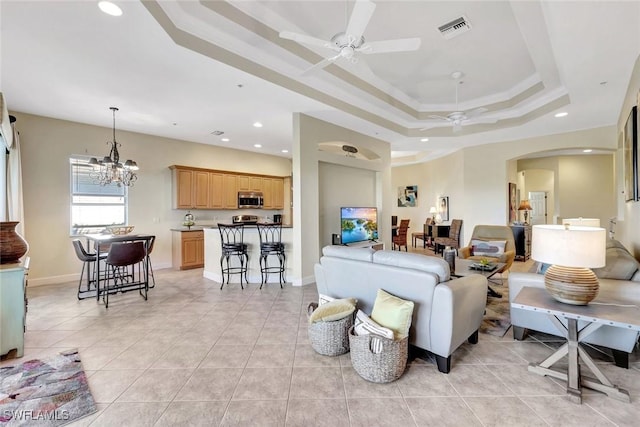 living area with a tray ceiling, light tile patterned floors, ceiling fan with notable chandelier, and arched walkways