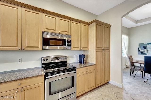 kitchen with light brown cabinets, stone countertops, arched walkways, appliances with stainless steel finishes, and light tile patterned floors