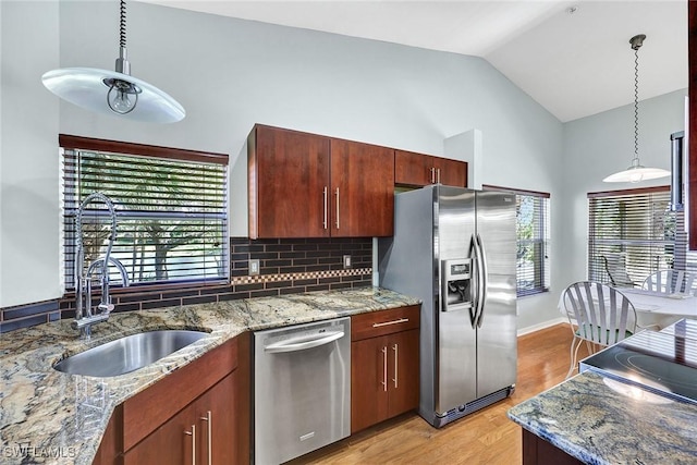 kitchen featuring a sink, stainless steel appliances, light wood-style floors, decorative light fixtures, and tasteful backsplash