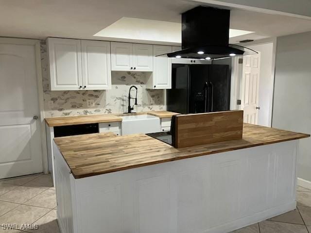 kitchen featuring wooden counters, light tile patterned floors, island exhaust hood, black fridge with ice dispenser, and a sink