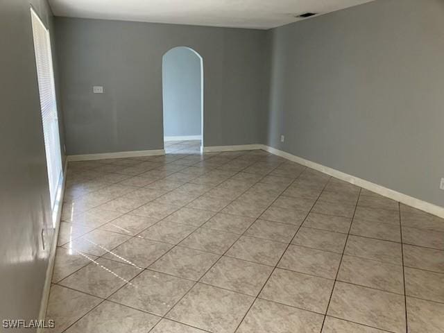 spare room with light tile patterned floors, baseboards, arched walkways, and visible vents