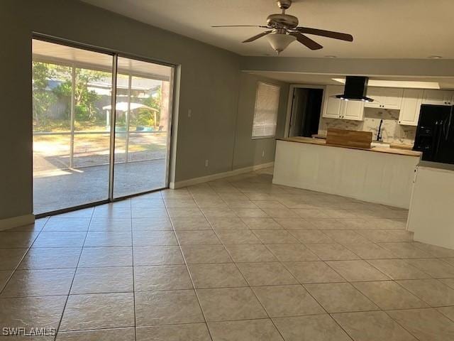 unfurnished living room featuring a sink, light tile patterned floors, baseboards, and ceiling fan