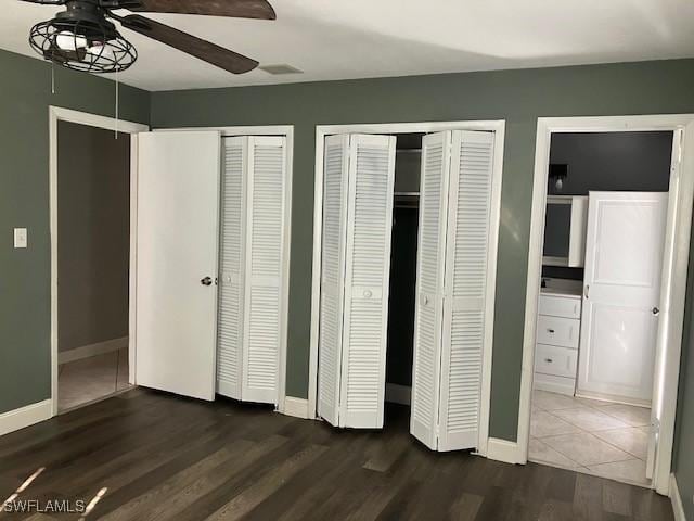 unfurnished bedroom featuring ceiling fan, baseboards, multiple closets, and dark wood-style flooring