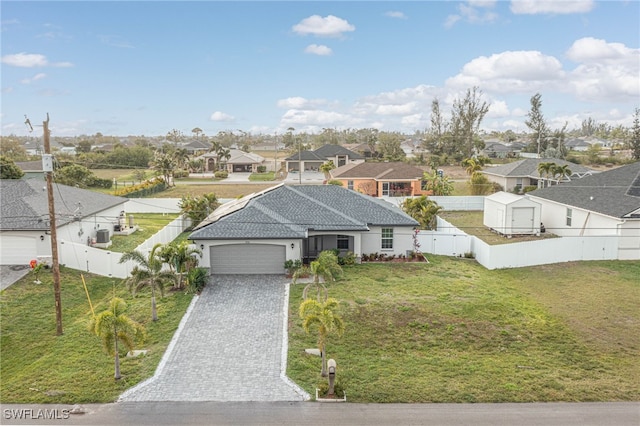 view of front facade featuring a residential view, a front yard, decorative driveway, a fenced backyard, and an attached garage