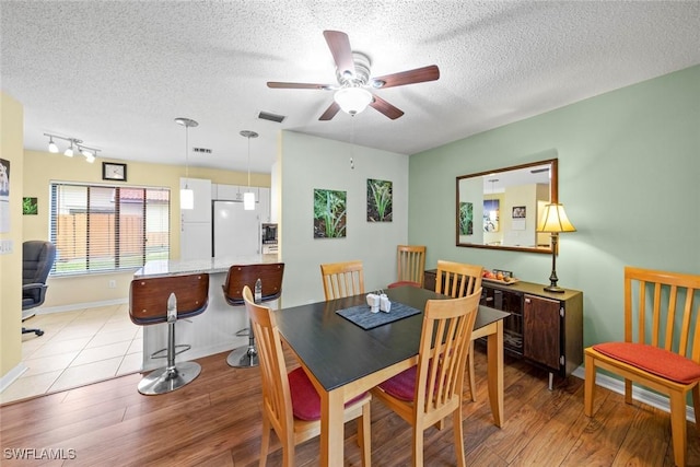 dining room featuring light wood-type flooring, visible vents, a ceiling fan, a textured ceiling, and baseboards