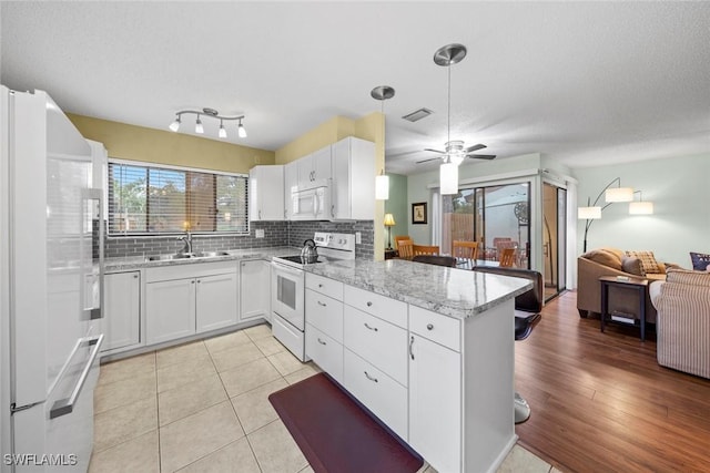 kitchen with visible vents, a sink, backsplash, white appliances, and a peninsula