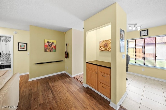 hallway with baseboards, track lighting, a textured ceiling, and light wood-style floors