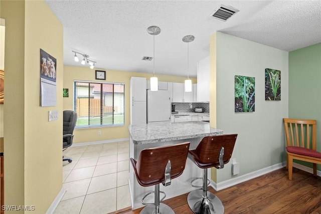 kitchen with a breakfast bar area, visible vents, white fridge, white cabinetry, and backsplash