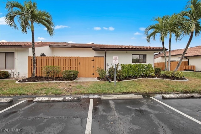 view of front of property featuring fence, a tiled roof, a gate, stucco siding, and uncovered parking