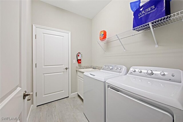 laundry area featuring a sink, washing machine and dryer, cabinet space, light wood finished floors, and baseboards