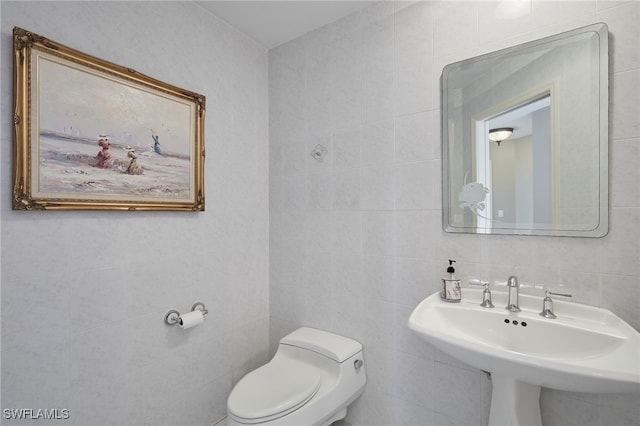 bathroom with tile walls, toilet, and a sink