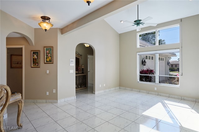 unfurnished room with light tile patterned floors, a ceiling fan, baseboards, high vaulted ceiling, and arched walkways