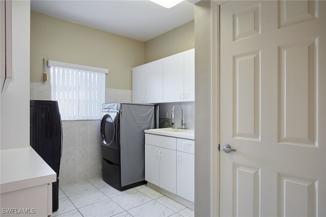 clothes washing area with a sink, cabinet space, tile walls, and washer and clothes dryer