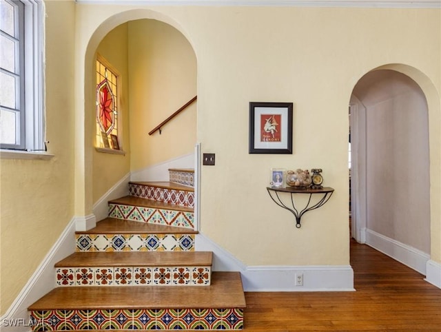 stairs featuring wood finished floors, arched walkways, and baseboards