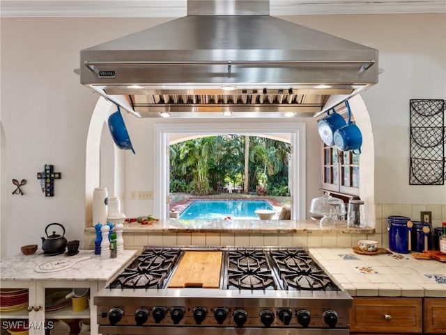 kitchen with brown cabinets, crown molding, extractor fan, and stainless steel gas stovetop