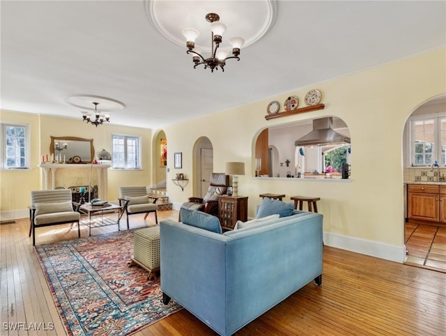 living area featuring a chandelier, arched walkways, baseboards, and light wood-style floors