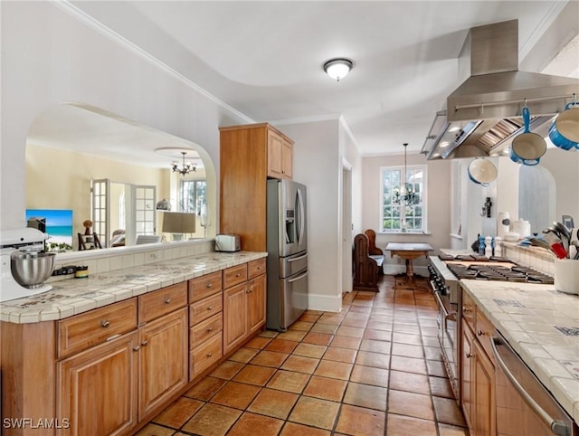 kitchen featuring arched walkways, stainless steel appliances, wall chimney range hood, open floor plan, and a chandelier