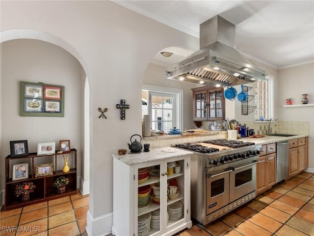 kitchen with crown molding, appliances with stainless steel finishes, island range hood, arched walkways, and a sink