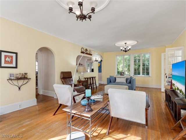 living area with an inviting chandelier, light wood-style flooring, baseboards, and arched walkways