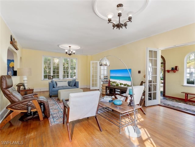 living area with arched walkways, baseboards, light wood-type flooring, and an inviting chandelier