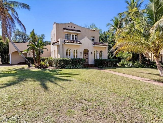 mediterranean / spanish home with stucco siding, a tile roof, and a front lawn