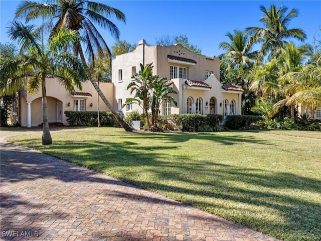 mediterranean / spanish house with a front yard, a tile roof, and stucco siding