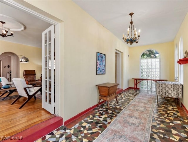 corridor featuring arched walkways, baseboards, an inviting chandelier, and wood finished floors