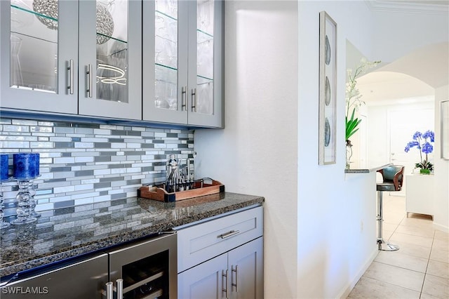 bar with beverage cooler, backsplash, arched walkways, light tile patterned floors, and a dry bar