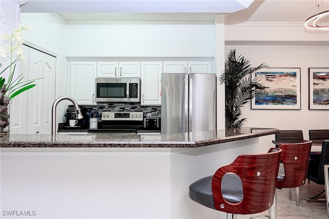 kitchen featuring a breakfast bar, dark stone counters, decorative backsplash, appliances with stainless steel finishes, and white cabinets