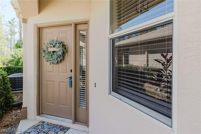 view of exterior entry featuring stucco siding and cooling unit