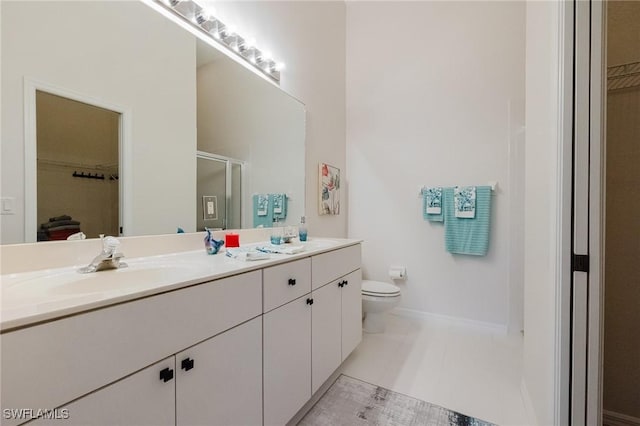 bathroom featuring double vanity, a sink, a shower stall, a walk in closet, and toilet