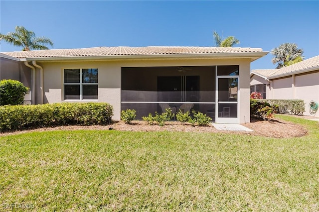 rear view of property with stucco siding, a sunroom, a lawn, and a tile roof