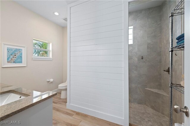 full bathroom with toilet, a tile shower, recessed lighting, wood finished floors, and vanity