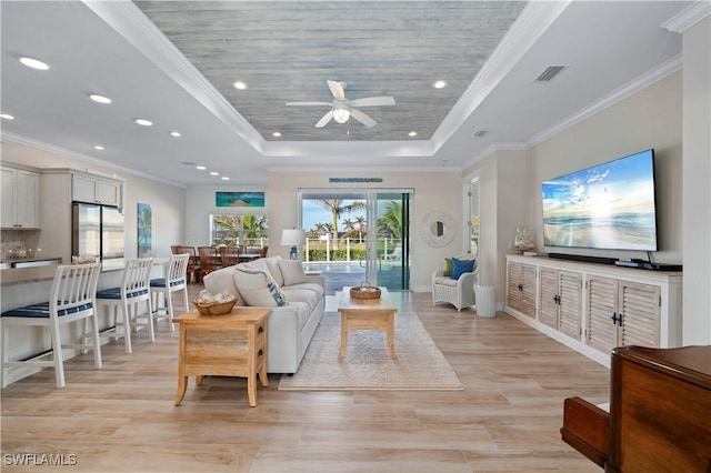 living room featuring visible vents, a tray ceiling, ornamental molding, recessed lighting, and light wood-style flooring