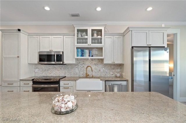 kitchen with visible vents, crown molding, light stone countertops, stainless steel appliances, and a sink