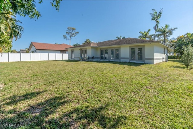 back of property with stucco siding, a lawn, french doors, and fence