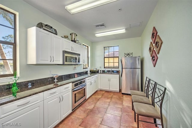 kitchen featuring visible vents, white cabinets, appliances with stainless steel finishes, and dark stone counters