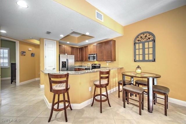 kitchen featuring a kitchen bar, visible vents, light stone counters, stainless steel appliances, and a peninsula