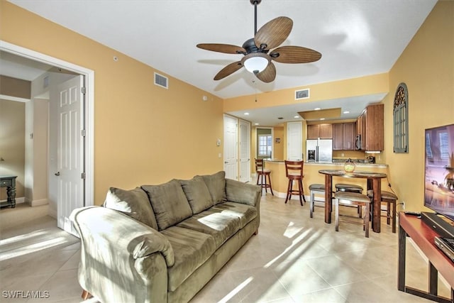 living room featuring light tile patterned floors, visible vents, baseboards, and a ceiling fan