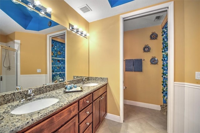 bathroom with a wainscoted wall, a shower stall, visible vents, and a sink