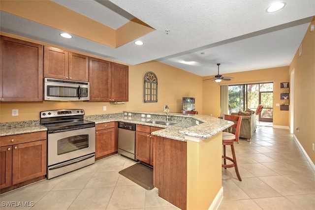 kitchen featuring a peninsula, a kitchen breakfast bar, brown cabinetry, stainless steel appliances, and a sink