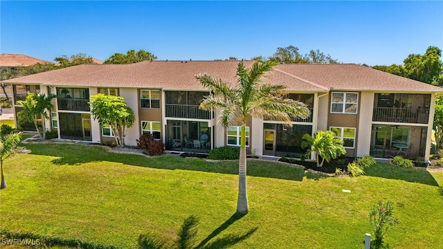 rear view of house featuring stucco siding, a lawn, and a sunroom