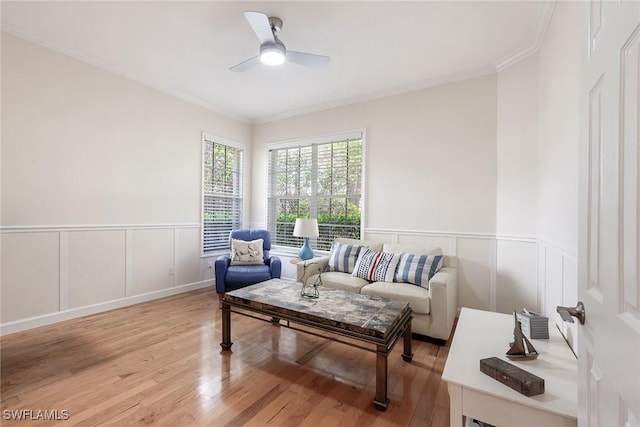 living area with a wainscoted wall, a ceiling fan, light wood-style flooring, and crown molding